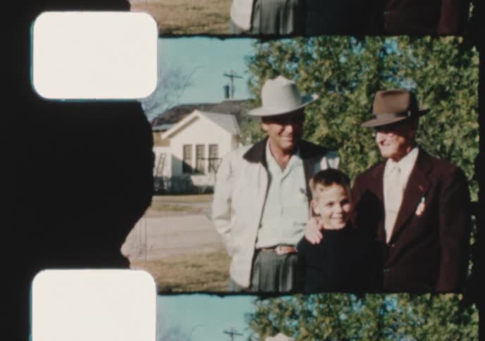 A vintage film captures a heartwarming family portrait of a grandfather, father, and son posing together outdoors