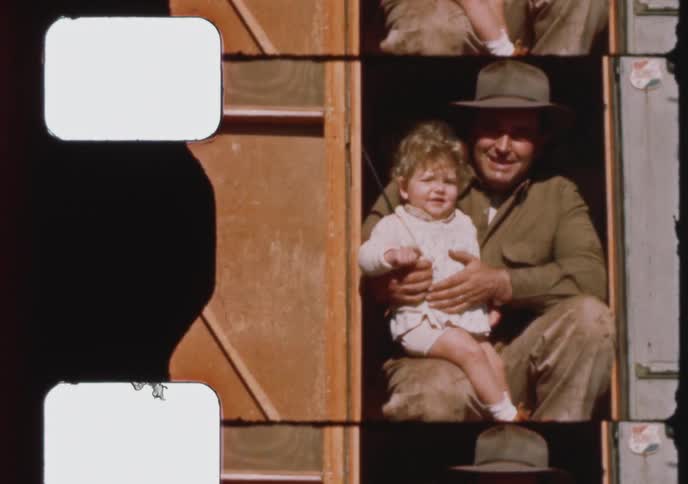 A father holds his toddler in the doorway of their trailer home in this archival 1940s home movie