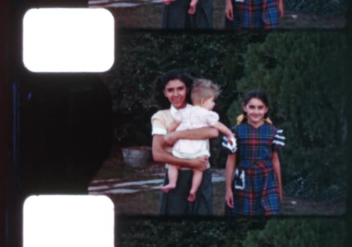 An archival home movie from the 1940s shows a teenage girl holding a baby and posing with her younger sister in a garden