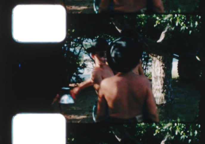 Three cool young boys with sunglasses put their arms around each other and pose for a vintage home movie