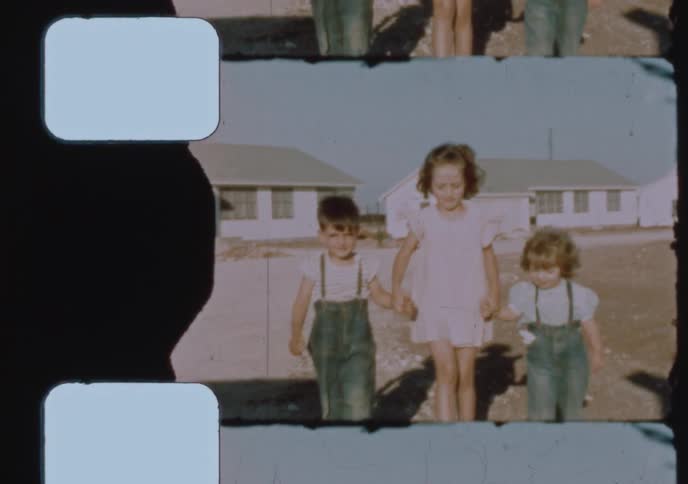 Charming 1940s home movie footage shows three young siblings holding hands as they walk towards the camera in a dusty yard