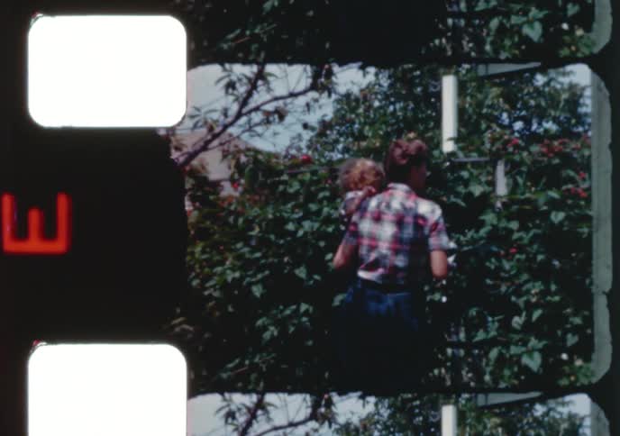 Vintage 1950s footage of a mother and her young child picking fresh berries from a bush in a sunny backyard garden