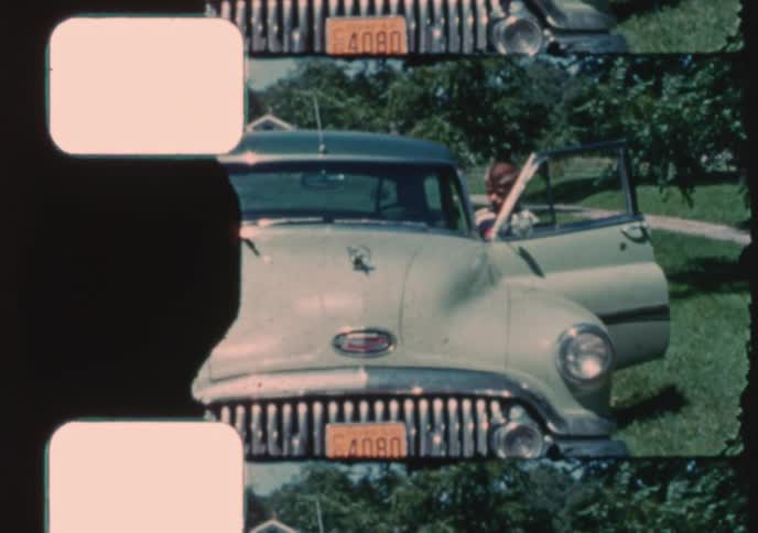 A classic 1950s Buick sedan is parked on the street as children happily get out of the car in this authentic vintage home movie