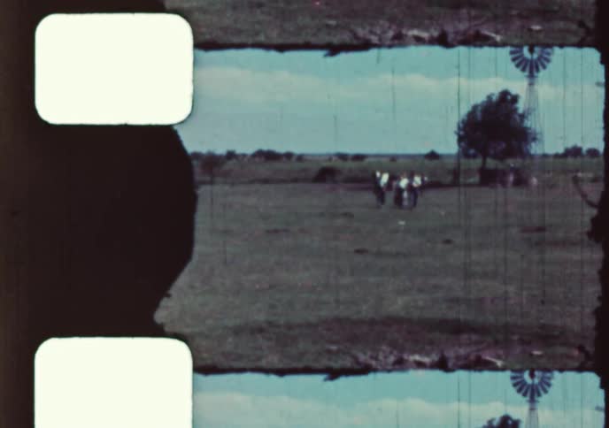 Vintage 16mm film captures a group of young boys walking across a rural farm pasture with a classic windmill in the background