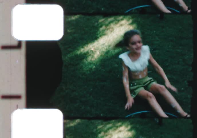 Vintage 8mm footage shows a playful young girl doing cartwheels on the grass before her mother teaches her how to use the camera