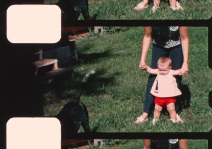 A mother helps her baby take its first steps in a sunny backyard on a beautiful day, captured on vintage film