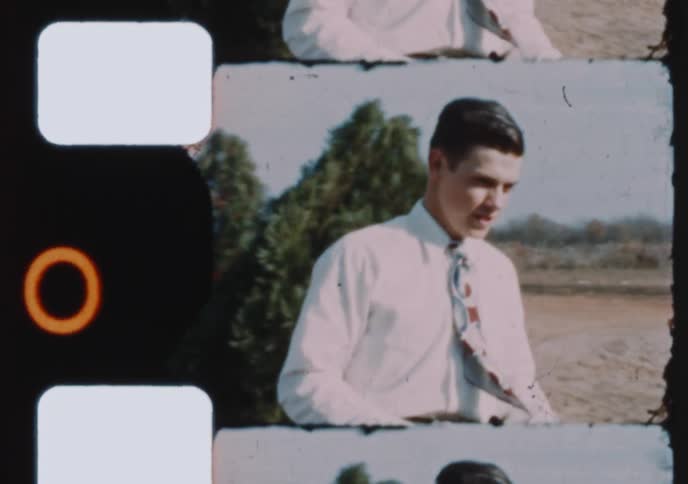 A young man dressed in a button-down shirt and tie stands in a rural yard in this nostalgic vintage home movie footage
