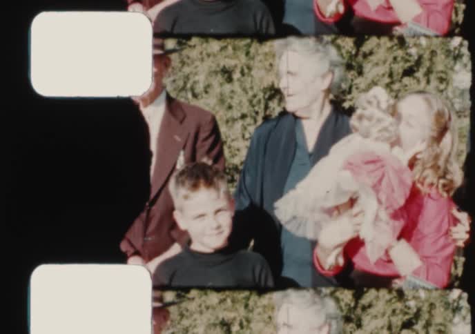 An 8mm film scan captures a multi-generational family posing together for an outdoor portrait in the 1950s