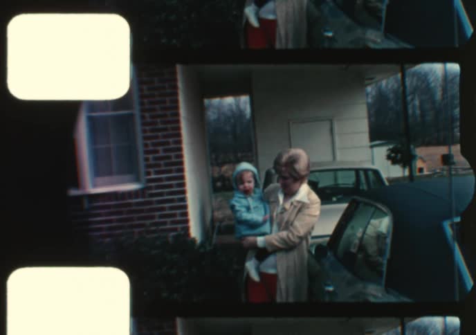 Vintage 8mm footage shows a proud mother holding her young child in the driveway of their suburban home
