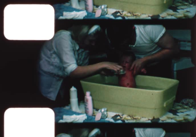 Authentic vintage footage shows parents tenderly bathing their crying newborn baby in a small plastic tub at home