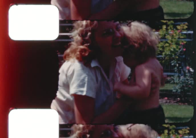 Vintage 8mm footage captures two women playing with a cute, curly-haired toddler in a sunny backyard rose garden