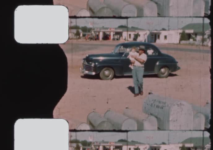A father gets out of his classic 1940s car and picks up his baby in a dusty, rural American town