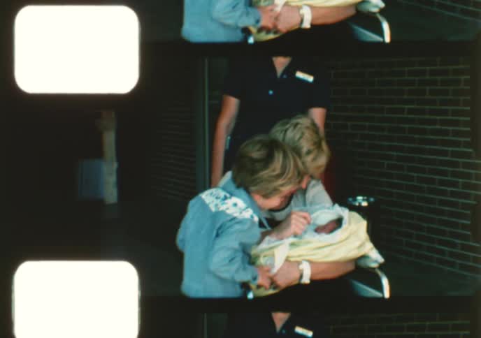 Vintage film captures a heartwarming family moment as a mother and her son admire their newborn baby while being wheeled out of the hospital