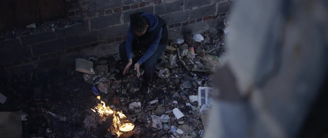 Woman sitting by a fire in an alleyway