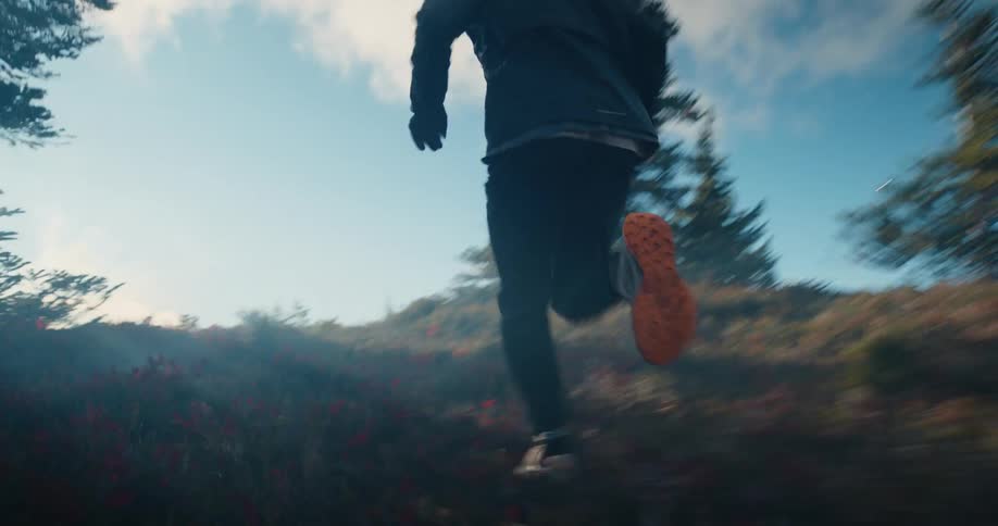 Dynamic low-angle follow shot of an athlete's feet as they run uphill on a scenic mountain trail towards the bright morning sun