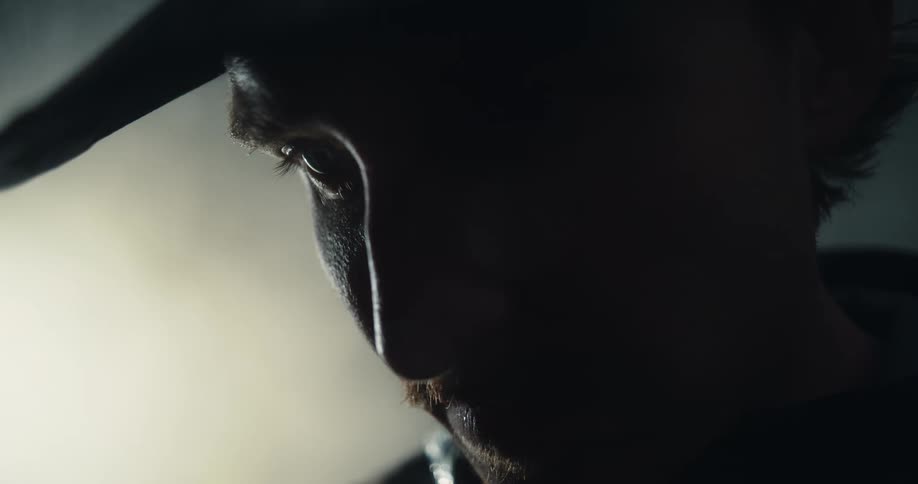 Dramatic close-up profile of a serious cowboy with a mustache looking down intently in a dark, smoky room