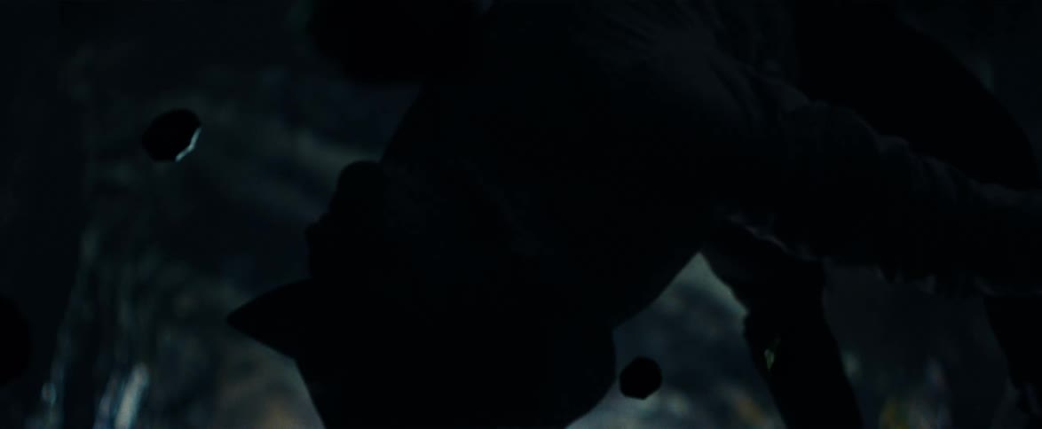A silhouetted figure is suspended upside down in a dark, abstract void as small particles float past in slow motion