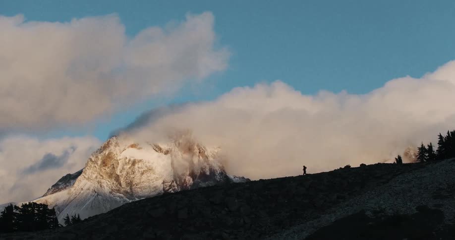 A runner's silhouette crosses a mountain ridge as the camera pans to reveal a vast, snow-capped peak shrouded in clouds