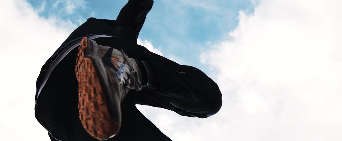 A dramatic slow-motion shot from a low angle captures the silhouette of a runner mid-stride against the sky