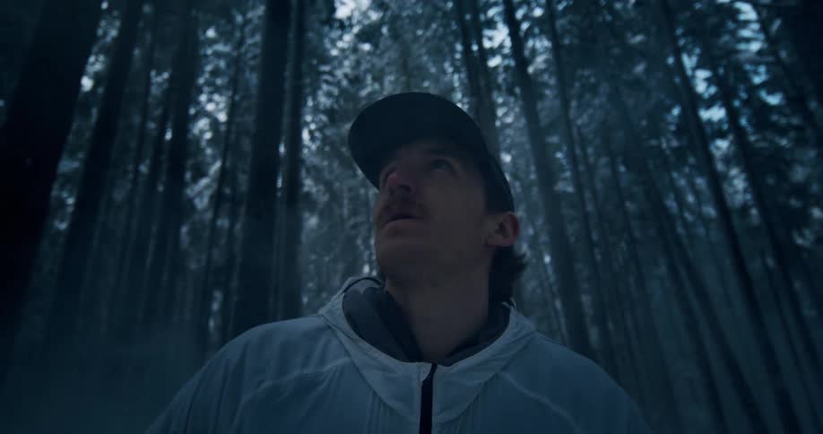 A hiker with a headlamp takes in the view of a mysterious, misty, snow-covered forest from a low angle