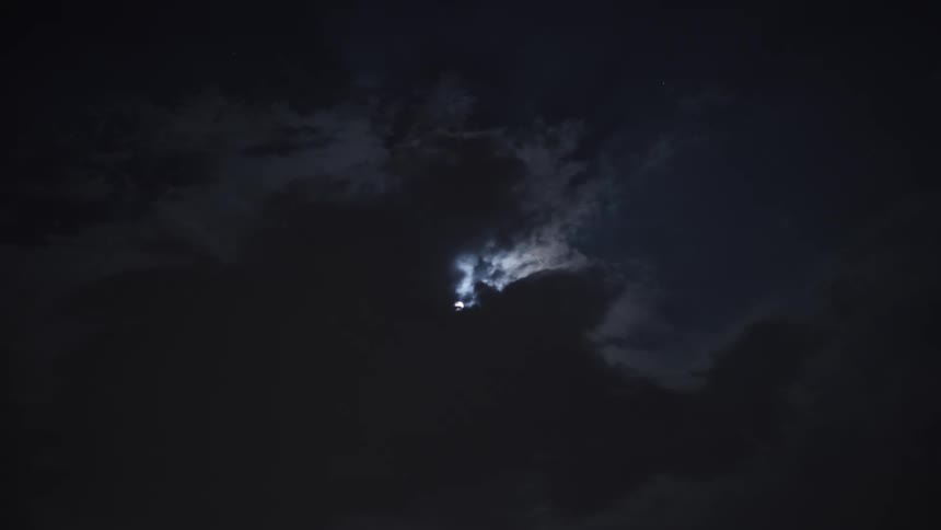 Lightning flashes from within dark storm clouds as the moon peeks through on a spooky night
