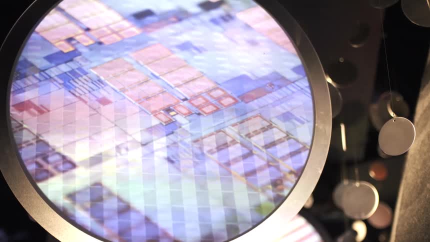 An abstract digital animation shows the intricate patterns and layers of a computer microchip wafer on a circular screen