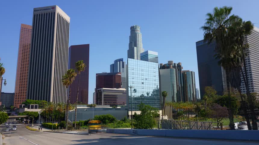 A daytime time-lapse zooms in on the iconic downtown Los Angeles skyline with busy traffic and palm trees