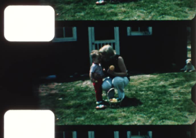 A vintage 8mm film captures a mother and her young child enjoying an Easter egg hunt in the yard of their country home
