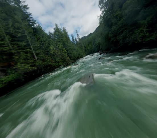 An immersive FPV drone shot flies low and fast over the turbulent green water of a river surrounded by a dense forest