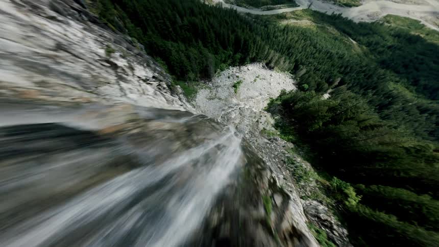 A thrilling aerial point-of-view dive down a cascading waterfall on a rocky mountain cliff into a lush green valley