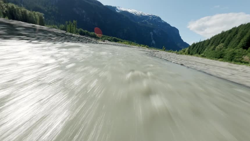 An exhilarating FPV drone flight speeds along a fast-flowing glacial river through a remote mountain valley