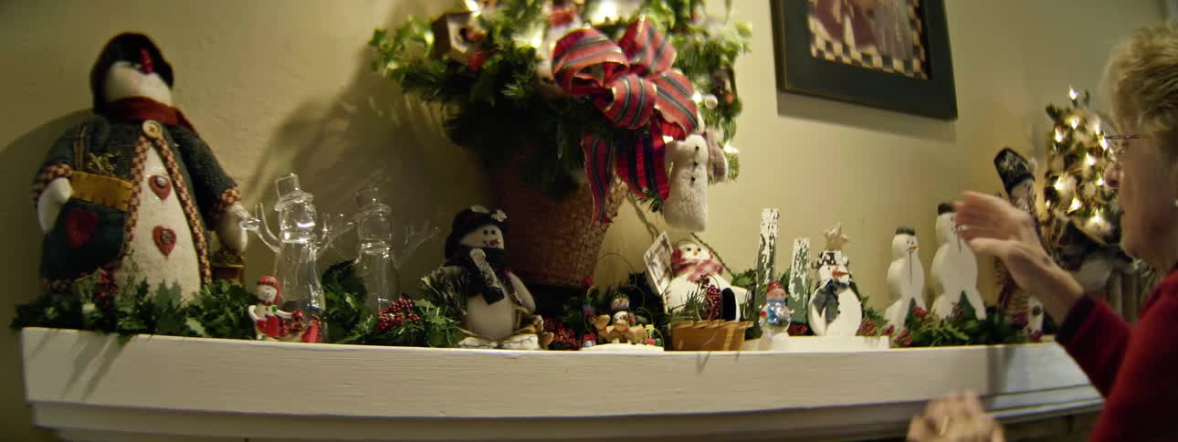 A woman straightens the christmas decorations on the mantel