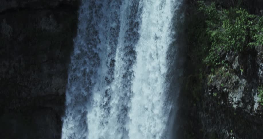 A powerful waterfall cascades over a dark, rocky cliff surrounded by a lush green forest