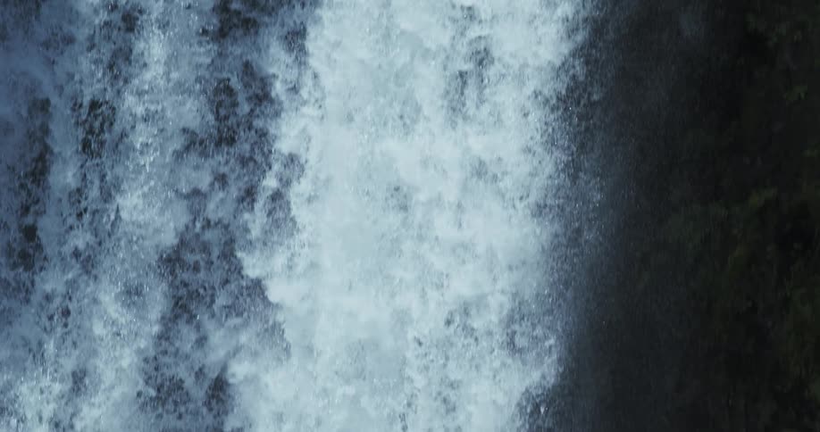 A slow motion close-up view of a waterfall as the water cascades down a dark rock face