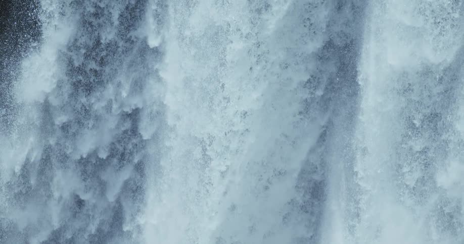 An abstract vertical close-up of a waterfall with turbulent white water falling in slow motion