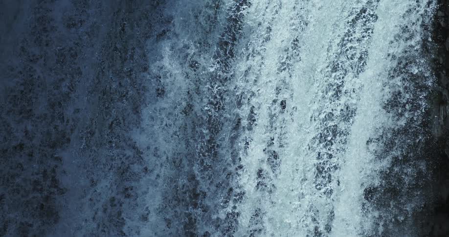 A powerful waterfall crashes down a dark rock face in a mesmerizing slow-motion vertical shot
