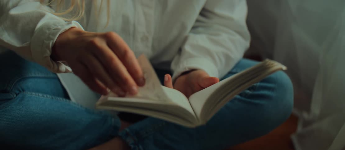 A serene blonde woman enjoys a quiet moment, turning the pages of a book in slow motion while sitting on the floor in a cozy room