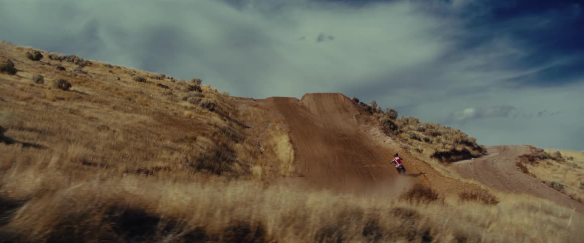 Dramatic slow motion shot of a motocross rider going up a steep dirt hill in a grassy, remote landscape