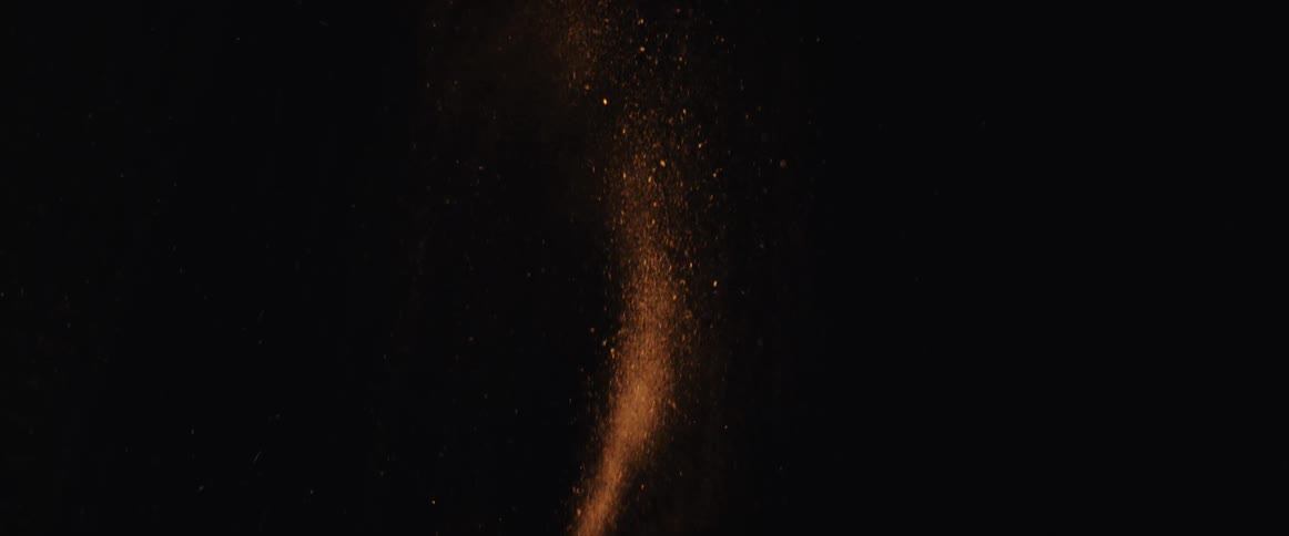 A sparkling stream of copper-colored dust and glitter falls gently in slow motion against a dark background