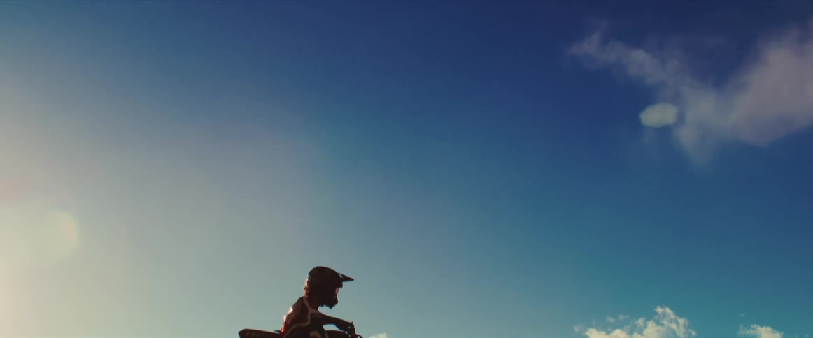 A motocross rider in silhouette flies through the air in super slow motion against a clear blue sky