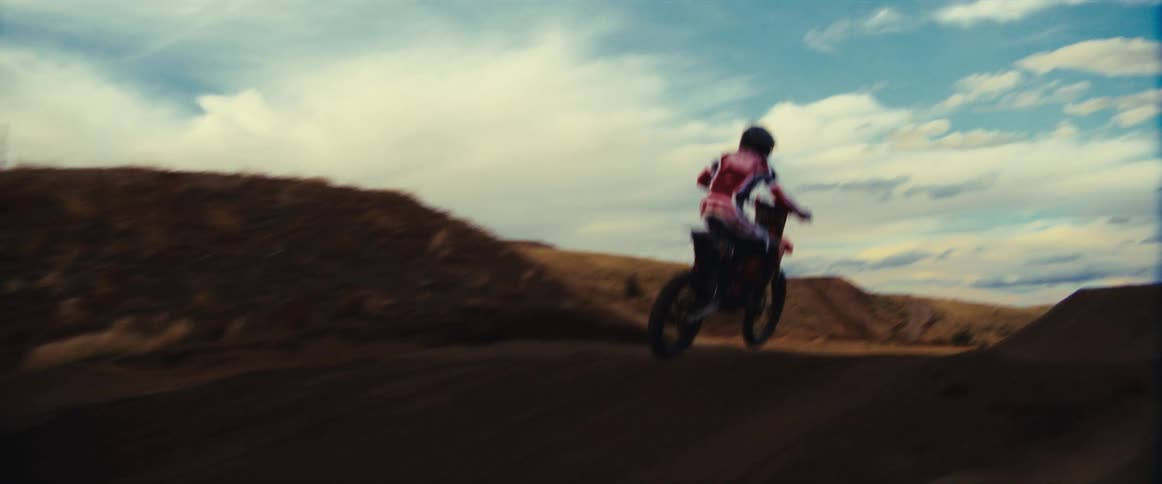 A motocross rider speeds along a dirt track before launching into the air in epic slow motion