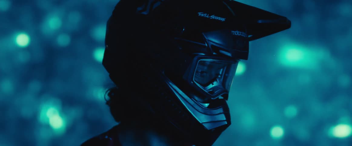 Cinematic close-up profile of a motocross rider in a helmet, illuminated by moody blue light against a bokeh background