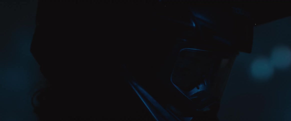 A close-up of a person in a motocross helmet at night, with their face hidden by goggles and illuminated by mysterious blue city lights