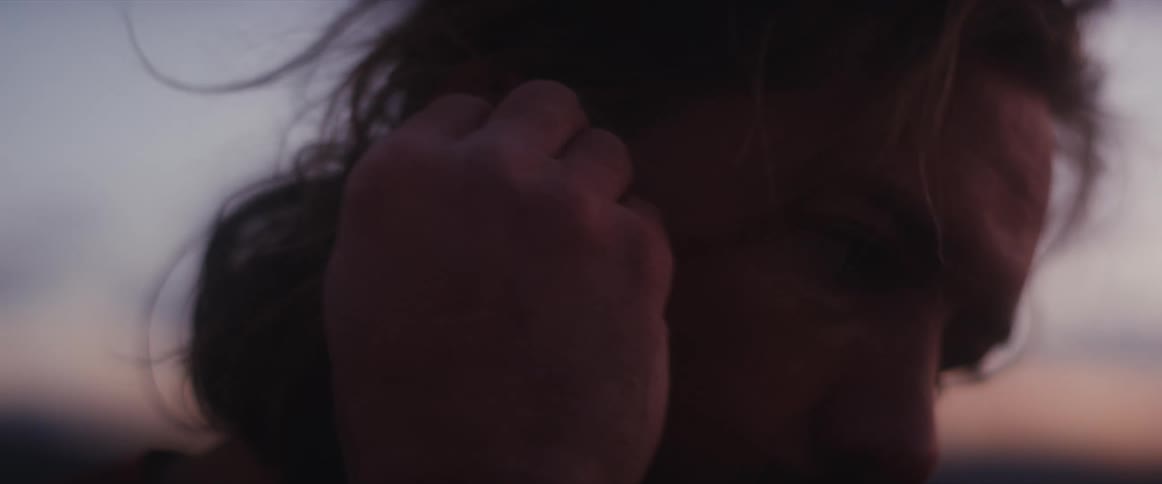 Extreme close-up of a man putting a wireless earbud in his ear against a soft sunset sky