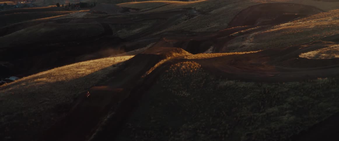 An aerial view shows a motocross rider in slow motion jumping on a dirt track during a beautiful golden hour sunset