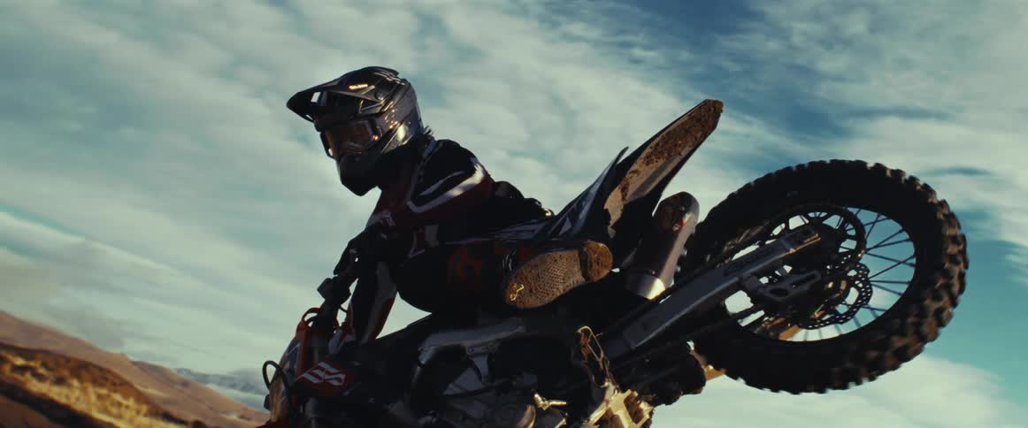 A motocross rider performs a daring mid-air stunt in dramatic slow motion against a vast, cloudy sky