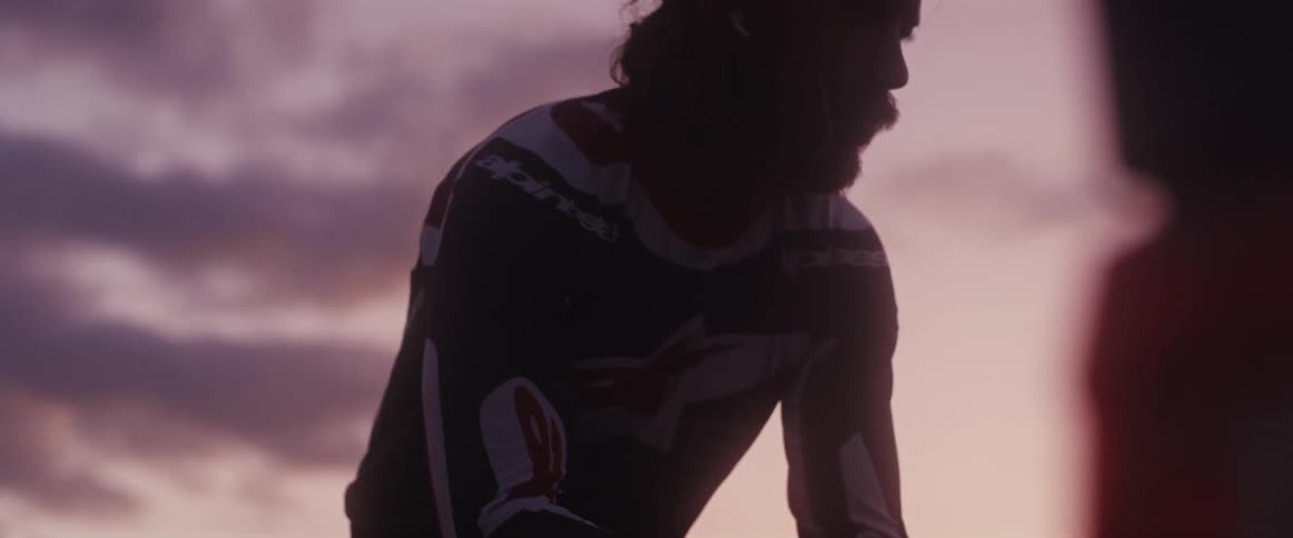 Close-up of a silhouetted male rider in racing gear sitting pensively during a beautiful sunset