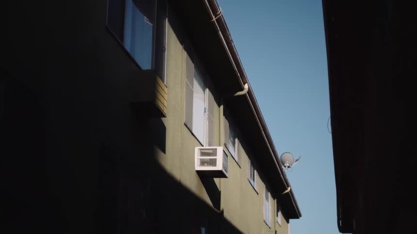Slowly panning down from the shadows to reveal an apartment building and a clear blue sky from a narrow alley