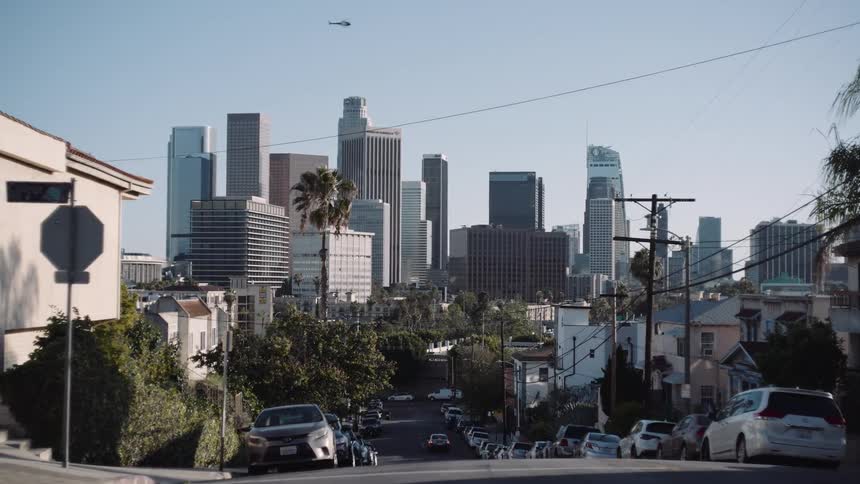 A slow cinematic pan reveals the iconic downtown Los Angeles skyline from a quiet, hilly residential street on a bright sunny day