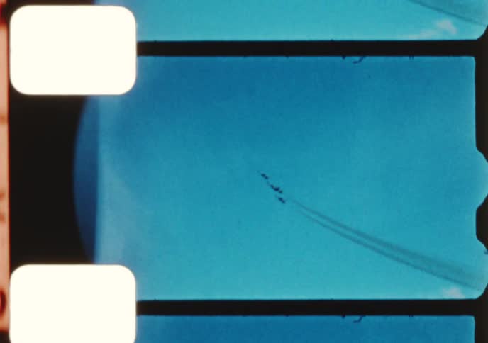 Vintage film shows a crowd watching as military jets perform aerobatic maneuvers in formation at an airshow